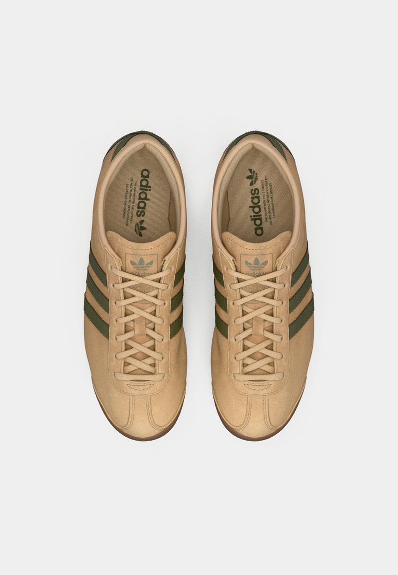 Paar hellbraune Adidassneaker aus Wildleder mit dunkelgrünen Streifen und Schnürsenkeln, von oben auf weißem Hintergrund betrachtet.