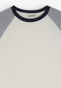 T-shirt blanc à col rond avec des manches raglan grises et un col bleu marine ; fabriqué en tissu doux avec une texture lisse. Comprend l'étiquette de la marque à l'intérieur.