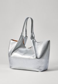 Zilveren leren tote bag met een gestructureerd oppervlak, twee handvatten en een open bovenkant. Heeft een contrasterende tan interieur en ronde uitsnijdetails.