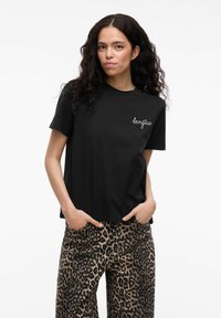 T-shirt in cotone nero con maniche corte, con la scritta "bonjour" in bianco sul petto; abbinato a pantaloni larghi con stampa leopardo.