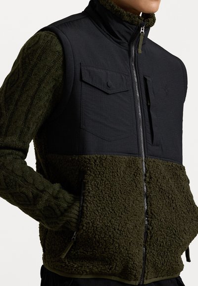 Melnā un zaļā veste ar teksturētu, pūkainu apakšējo daļu. Iekļauj rāvējslēdzēja aizdari, divas krūšu kabatas un augstu apkakli no mīksta materiāla.