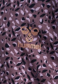 Tissu violet avec un motif léopard comportant des taches noires et roses claires. Un logo "hummel" en bronze est positionné en bas.