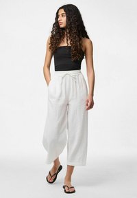 Pantalons larges blancs en tissu texturé, avec une taille élastique et un cordon de serrage. Associés à un haut noir ajusté et des tongs noires.
