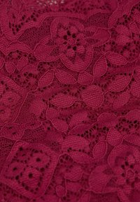 Tessuto in pizzo bordeaux con motivi floreali, caratterizzato da texture intricate e trame aperte, che mostrano cuciture dettagliate ed elementi in rilievo.