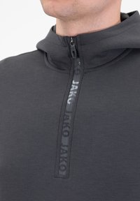 Pullover grigio scuro con colletto zip, caratterizzato da una stampa del logo. Il materiale appare liscio e elastico, con una sottile texture.