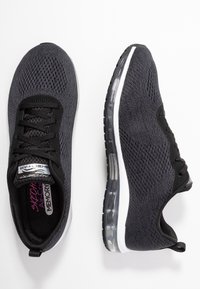 Svarta sportskor med mesh-övre, snörning och genomskinlig luftdämpande sula. Mönstrad textur och vadderad krage.