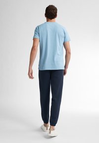 Lichtblauwe t-shirt met korte mouwen, donkerblauwe joggers, witte sneakers met tan accenten, eenvoudige stijl, zachte textuur, comfortabele pasvorm.