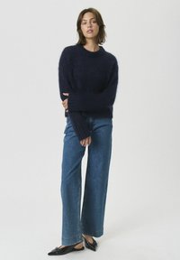 Navy blue knitted sweater with a crew neck and long sleeves, paired with wide-leg denim jeans and black flat shoes.