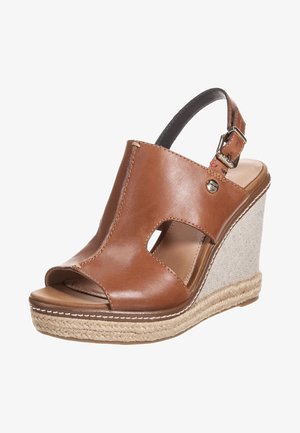 Brązowe skórzane sandały na koturnie z odkrytymi palcami. Posiadają pasek na kostkę, teksturowaną beżową platformę oraz dekoracyjne detale w postaci przeszyć.