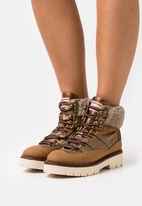 Brown lace-up boots with a textured fabric collar, rubber sole, metal eyelets, and contrasting cream platform; designed for durability.