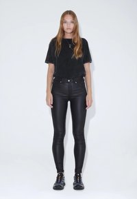 Černé semišové tričko s krátkými rukávy v kombinaci s černými úzkými džíny s vysokým pasem. Obuv tvoří černé a šedé sportovní boty.