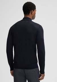 Granatowy sweter typu pullover z długimi rękawami, prążkowanym kołnierzem i mankietami, o gładkiej fakturze i dopasowanym kroju, widziany od tyłu.