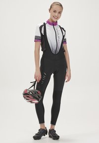Fietsbretels in het zwart met een strakke pasvorm, voorzien van een textuurpatroon in wit en paarse accenten. Houdt een rood en zwart helm vast.