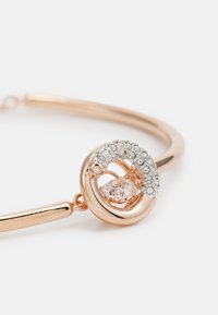 Armband aus Roségold mit einem verdrillten Design und einem zentralen klaren Edelstein, umgeben von kleinen, funkelnden Strasssteinen. Glatte Metalloberfläche.