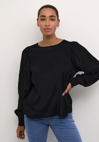 Black long-sleeve top with a round neckline, textured fabric, pleated shoulders, and gathered cuffs, paired with mid-blue jeans.