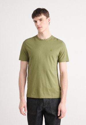 Olijfgroene katoenen t-shirt met een ronde hals en korte mouwen. Heeft een subtiele logo op de linkerborst. Gecombineerd met donkere jeans.