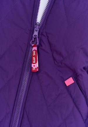 Fioletowa pikowana kurtka z zamkiem błyskawicznym z przodu, z czerwoną tkaninową zakładką z napisem "ŻYJ ZE MNĄ" oraz różową metką z boku.