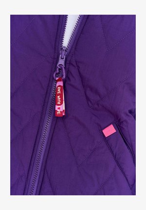 Fialová prešívaná bunda s predným zipsom, s červenou látkovou popiskou označenou "ŽI S MOU" a ružovou visačkou po boku.