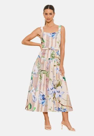 Donna che indossa un vestito midi beige senza maniche con righe verticali e grandi motivi floreali blu e verdi, abbinato a sandali beige con tacco.