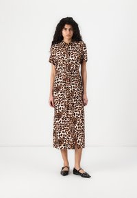Abito camicia a stampa leopardata con maniche corte, vita cintrata e lunghezza al ginocchio. Abbinato a scarpe basse nere con punta affusolata.