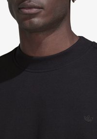 Svart sweatshirt med ribbad nackkrage. Har en liten, svart broderad logotyp på bröstet. Slitstark tygstruktur.