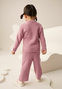 Rosa gestrickter Pullover und passende Hose aus weichem Material, mit gerippten Bündchen und Saum. Das Set hat eine lockere Passform und minimale Details.