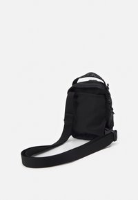 La borsa a tracolla nera in tessuto presenta una forma rettangolare, una tracolla regolabile e una chiusura a zip con dettagli in metallo decorativi.