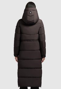 Pruunist paddinguga pikk kasukas kapuutsiga, millel on horisontaalsed tikkimisosad ja ümmargune nööbikas detail kaela juures ning elastsed mansetid.