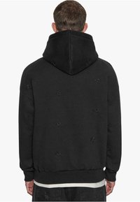Schwarzer Hoodie mit einem strukturierten Muster, ausgestattet mit einer verstellbaren Kapuze und gerippten Bündchen. Hergestellt aus weichem Stoff mit einer lockeren Passform.