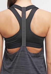 Zwarte sporttanktop met een racerback-ontwerp en een verbindingsbandje, gecombineerd met een grijze rug met golfpatroon. Zachte stoftextuur.