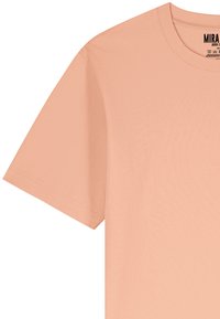 T-shirt à manches courtes de couleur pêche clair, fabriqué en coton doux, avec un col rond et une coupe décontractée. Design minimal sans motifs.