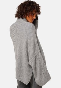 Pull en maille gris clair avec un col montant, coupe ample, manches texturées en tricot torsadé et fente sur le côté pour plus de liberté de mouvement.