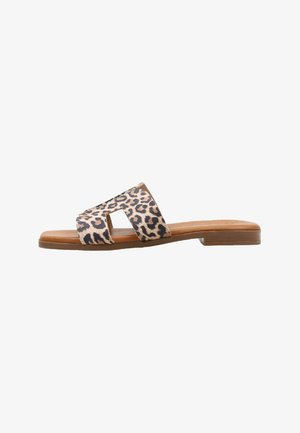 Sandalia plana tipo slide con suela marrón claro y tiras anchas de estampado de leopardo marrón con recortes geométricos sobre fondo blanco.