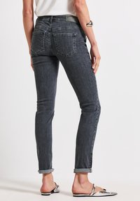 Jean ajustados en denim gris oscuro, con cintura de altura media, puños enrollados y bolsillos traseros. Textura suave con adornos mínimos.