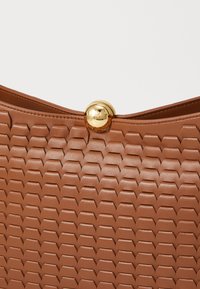 Brown textured leather bag with a geometric pattern and a glossy gold clasp. Smooth finish complements the intricate design.