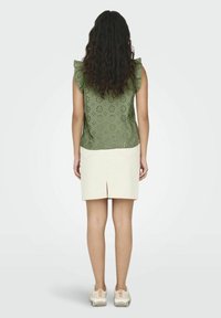 Top verde ricamato con maniche a volant, abbinato a una gonna crema con uno spacco posteriore e sneakers dai toni neutrali.