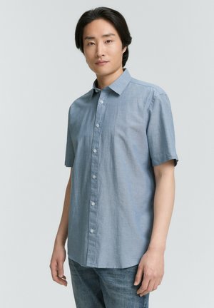 Lyseblå kortærmet skjorte i et blødt, tekstureret stof; har krave og knaplukning foran; parret med blå denim jeans.