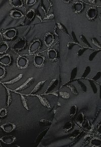 Tecido preto com intrincados bordados florais pretos, apresentando recortes circulares e padrões de folhas, criando uma aparência texturada.