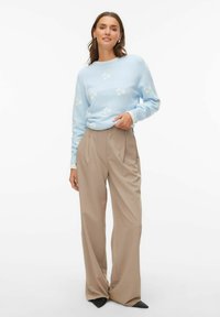 Jasnoniebieski sweter z białymi wzorami, połączony z beżowymi szerokimi spodniami. Miękka tekstura, luźny krój i subtelne detale w kształcie.