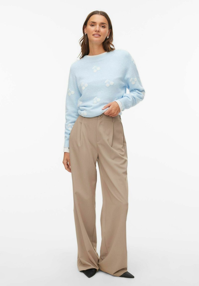 Jasnoniebieski sweter z białymi wzorami, połączony z beżowymi szerokimi spodniami. Miękka tekstura, luźny krój i subtelne detale w kształcie.