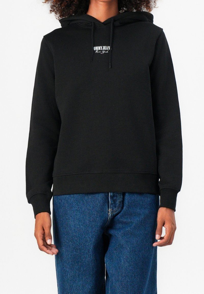 Sweat à capuche noir en tissu doux, avec une poche kangourou à l'avant et un petit logo sur la poitrine. Manches longues et poignets côtelés.