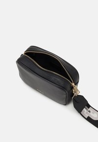 Černá kožená crossbody taška s texturovaným povrchem, zlatým zipem a nastavitelným popruhem. Obsahuje prostorný interiér a diskrétní logo.