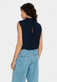 Top senza maniche blu navy con colletto alto e dettaglio a chiave sul retro, abbinato a pantaloni in denim azzurro chiaro con tasche sul retro e vestibilità ampia.