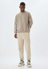 Sudadera beige con un ajuste relajado y cuello redondo, combinada con joggers beige claros y zapatillas chunky estampadas, sobre un fondo neutro.