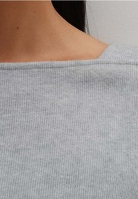 Grå ribbad stickad tyg med vid halsringning, som visar en jämn struktur och subtila färgvariationer. Lämplig för avslappnad användning.