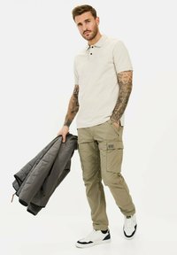 Lys beige polo skjorte med korte ærmer, parret med oliven cargo bukser med nytte lommer. Grå quilted jakke draperet over den ene arm.