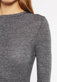 Grå teksturert genser med ribbestrikket design, med lange ermer og rund hals. Materialet har en subtil glans.