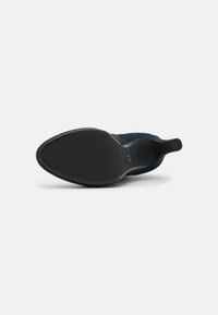 Zapato de ante azul marino con punta afilada y suela de goma negra lisa. Diseño minimalista sin hardware o patrones visibles.