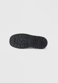 Talpa de pantof negru cu un model de profil rugos, având puncte de aderență ridicate și un logo central. Fabricată dintr-un material din cauciuc durabil.