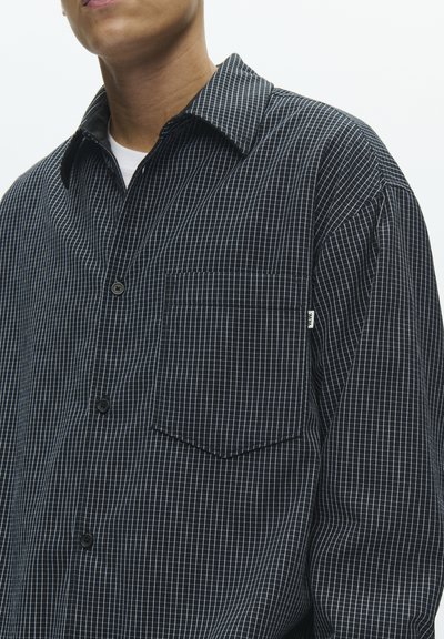 Sort- og hvidternet skjorte med knapper, spids krave, enkelt brystlomme og tekstureret stof. Sorte knapper og korte ærmer.